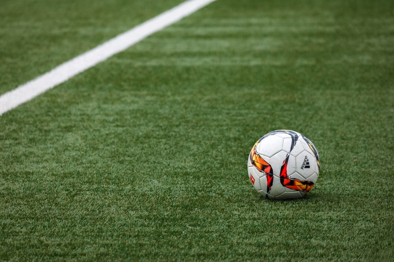 Pelota de futbol y botines sobre cesped sintetico en una cancha recreativa